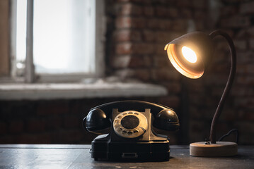 Old black rotary phone and lamp on the antique desk table background.