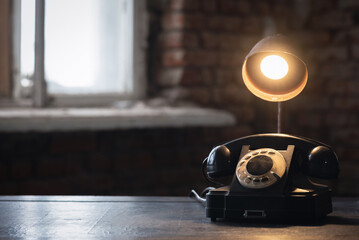 Old black rotary phone and lamp on the antique desk table background.