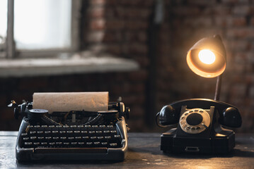 Old typewriter, rotary phone and lamp on the retro desk table background.