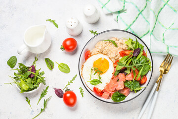 Savory breakfast. Oatmeal porrige with salted salmon, egg and fresh salad. Healthy food, balanced nutrition. Top view on white table.