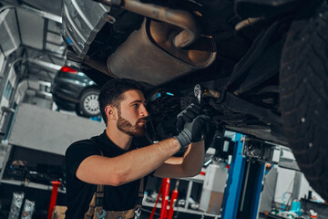 Fototapeta na wymiar Car mechanic examining car suspension of lifted automobile at repair service station.
