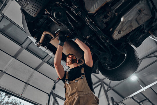 Car mechanic inspecting car wheel and suspension detail of lifted automobile at repair service station.