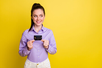 Photo portrait of cute girl looking at blank space holding credit card in two hands isolated on bright yellow colored background