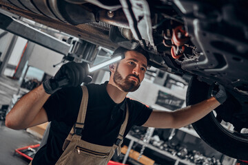 Portrait shot of a handsome mechanic working on a vehicle in a car service. Professional repairman...