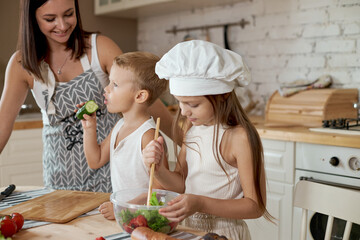Family prepares lunch in the kitchen. Mom teaches her daughter and son to prepare a Salad of fresh vegetables. Healthy natural food, vitamins for children