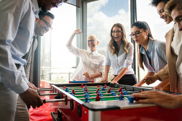 Employees playing table soccer indoor game in the office during break time