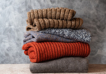 Pile of folded knitted warm women sweaters and scarves on gray background. Soft comfortable cozy...