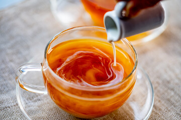 Pouring milk into cup with aromatic tea.