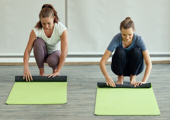 Two women rolling yoga mats after class with happiness