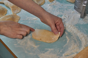Raw chebureks, calzone or qutab, with minced meat and onion in on the table. Woman's hands   in process of making homemade qutab or chebureki, calzone. Azerbaijani, Tatar, Caucasian, Greek cuisine. 