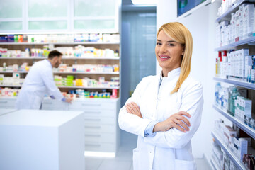 Obraz na płótnie Canvas Portrait of professional woman pharmacist proudly standing in pharmacy shop or drugstore. In background shelves with medicines. Healthcare and medicine.