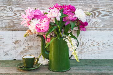 Beautiful bouquet of pink, purple peonies in green vintage coffee pot and cup of coffee on rustic wooden background