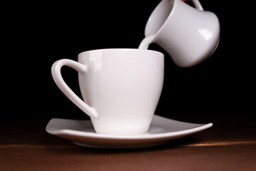 Pouring milk into a small cup of hot coffee.