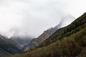 Snow capped mountain range in the clouds. Dense forest on the mountain slopes Caucasus, Russia