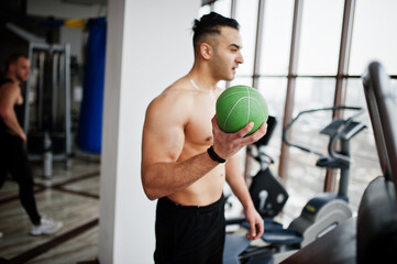 Muscular arab man training in modern gym. Fitness arabian men with naked torso doing exercises with ball.