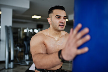 Fototapeta na wymiar Muscular arab man training in modern gym. Fitness arabian men with naked torso doing exercises with boxing bag.