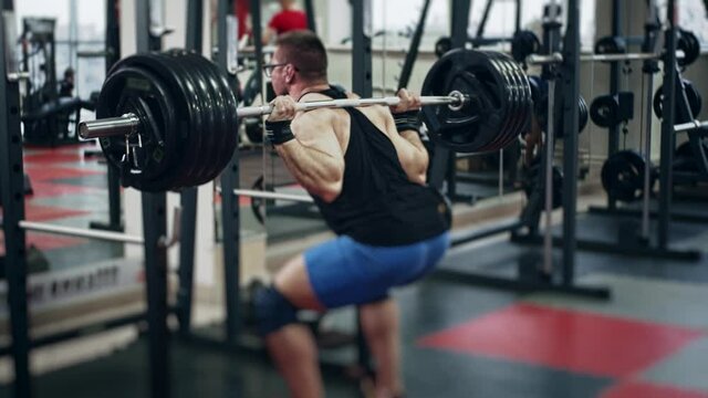 Young powerlifter in gym back squating, slow motion. Selective focus on barbell