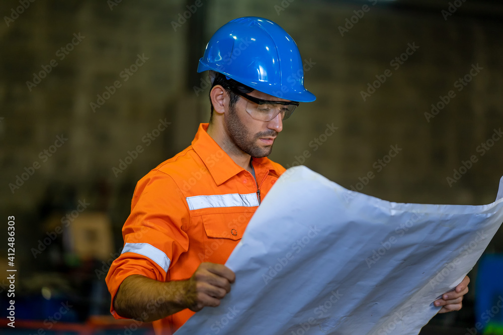 Fototapete engineer in factory watching blueprint for the working process.