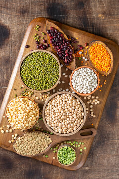 Different legumes. Mung beans, red and white beans, lentils, peas and chickpeas in wooden bowls on a brown wooden kitchen table. Beans close-up. Vegetarian food. Top view