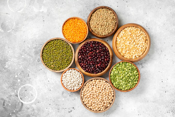 Different legumes. Mung beans, red and white beans, lentils, peas and chickpeas in wooden bowls on the light grey kitchen table. Top view 