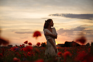 girl in a white dress in a field of poppies on a sunset background