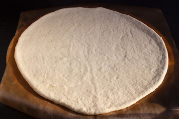 Raw dough for pizza on parchment paper on black background