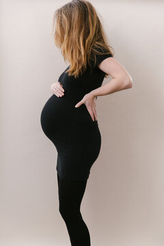A European caucasian pregnant woman in tight black outfit holding her belly.