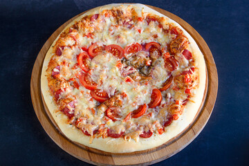 Pizza with pepperoni, tomatoes, mozzarella, on wooden board on black background. Valentines Day concept, soft focus