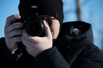 Photographer man in warm clothes in the winter holds the camera up close to my face taking pictures of nature. An article about winter photography, the use of photographic equipment in the cold season