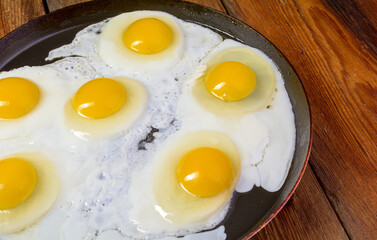 Fried eggs in a frying pan on an old rustic wooden table, top view.