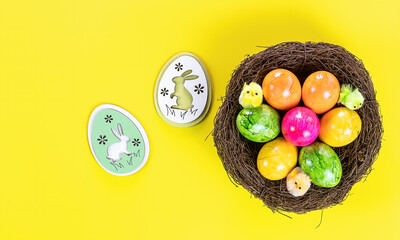 Easter eggs in nest and wooden decorative bunny on yellow background.