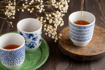View of three blue cups with tea, white flowers, selective focus, on green plate and wooden table, horizontal