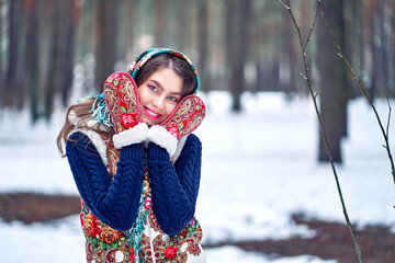 A woman in a winter forest in a bright scarf and warm mittens. National Russian clothing.