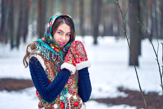 A woman in a winter forest in a bright scarf and warm mittens. National Russian clothing.