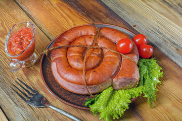 Smoked sausage, twisted in a spiral in a plate of herbs on an old rustic wooden table.Homemade food.Selective focus.