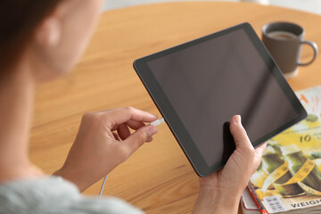 Woman connecting charger cable to tablet at wooden table, closeup