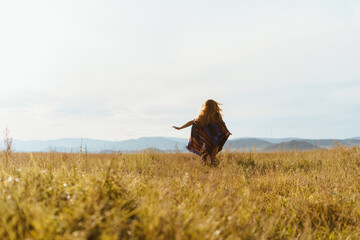 steppe and hills in the distance girl running away with her hands placed on the sides in a poncho on her shoulders, the wind inflates her hair. High quality photo