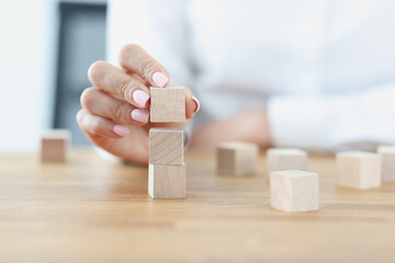 Female hand builds tower from wooden cubes. Building service business from scratch to market...