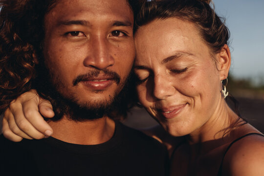 A woman closing her eyes and smiling blissfully hugs the neck of an East Asian man. High quality photo