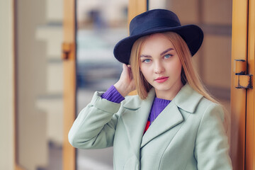 Portrait of a cute girl in a hat and coat looking at camera. business woman at the entrance to an office building. close up