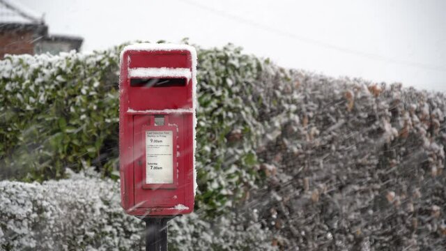 Village red postbox in falling snow