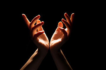 Fototapeta premium Beautiful folded hands with light on top, black background. Prayer or creating a miracle. Hand gestures
