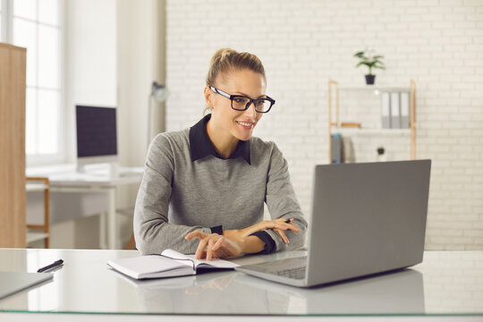Freelancer, distant working, elearning concept. Young smiling pretty woman worker sitting and looking at laptop screen during teleconference, videocall, online lecture. Distant learning, connection