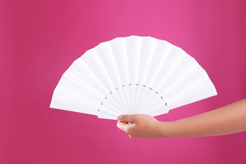 Woman holding white hand fan on pink background, closeup - obrazy, fototapety, plakaty
