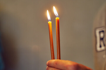Two lighted church candles in hand close-up.