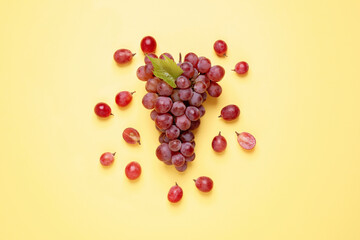 Bunch of ripe red grapes with green leaf on yellow background, flat lay