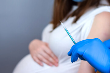 Doctor giving COVID -19 coronavirus vaccine injection to pregnant woman. Doctor Wearing Blue Gloves...