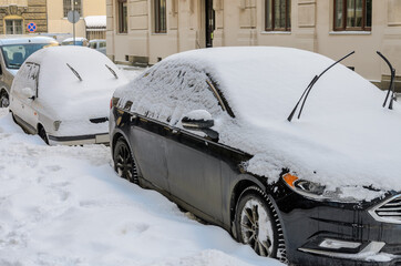 In winter, on a snow-covered street there are cars covered with snow
