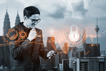 A young handsome eastern cybersecurity developer explores new approaches to protect clients confidential information using phone. IT lock icons over Kuala Lumpur city background. © VideoFlow