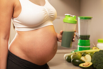 Pregnant woman holding shaker with a green protein cocktail